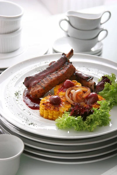 Ребра жареной баранины подаются с жареной кукурузой, салат, соус барбекю, на белой тарелке . — стоковое фото