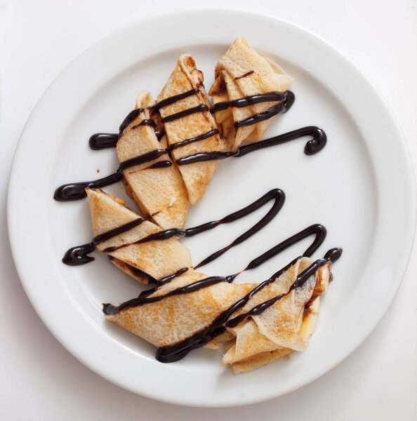 Тарелка вкусных блинов рулет со свежими фруктами и шоколадом на белой тарелке
