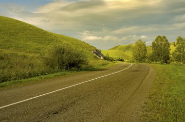 Ağaçlar ve bulutlu gökyüzü ile güzel yeşil yaz dağlarında Yol