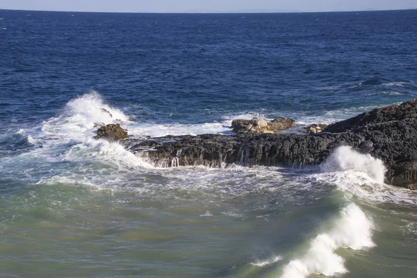 Foamy waves crashing against a stone cliff at high tide. Greece