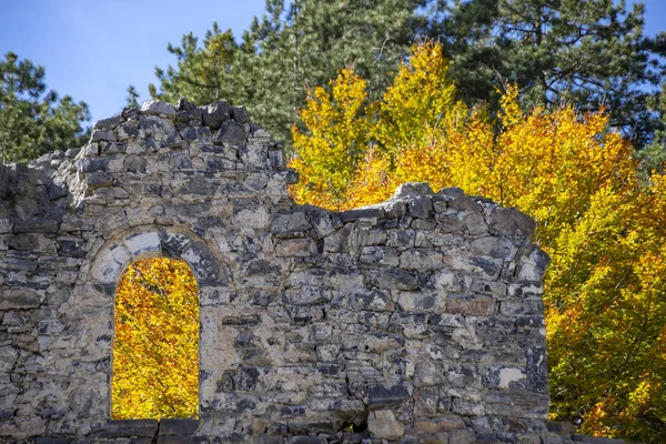Le mur d'un ancien bâtiment détruit. Dans la fenêtre et derrière le mur se trouvent des arbres au feuillage d'automne doré . — Photo
