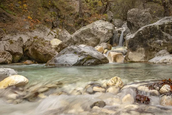 Waterfalls and a river between stone boulders are covered with moss in a mountain autumn forest. Greece