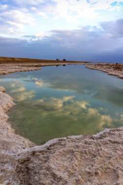 Bir bulutlu gökyüzü Lut gündoğumu, tuz formasyonları arasında su yansıması.