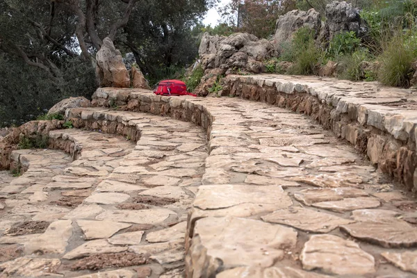 Mochila turística vermelha deitada em degraus de pedra com árvores grandes pedras no fundo — Fotografia de Stock