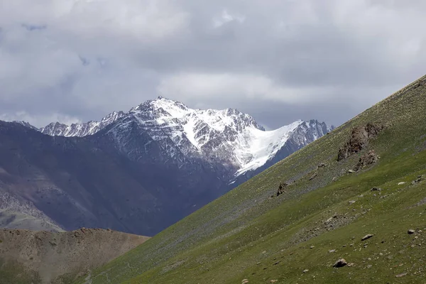 Groene heuvels en bergen met met sneeuw bedekte toppen tegen de hemel met wolken. Reizen in Kirgizië — Stockfoto