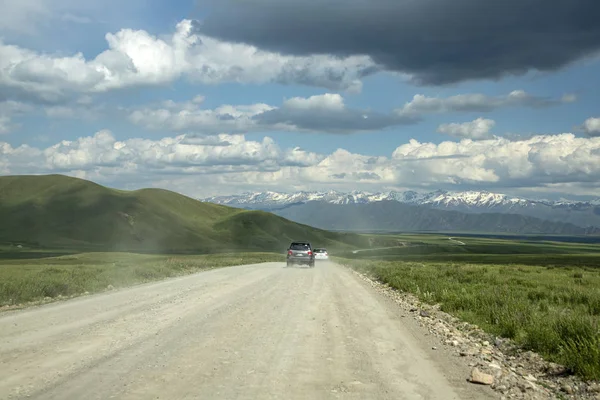 Cars traveling along the road of stresi of green fields and hills in the direction of the mountains