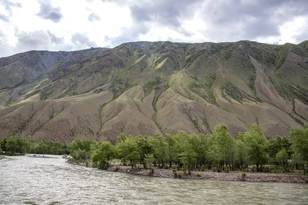 Rivier stroomt tussen schilderachtige heuvels. Bomen langs de oevers. Reizen in Kirgizië — Stockfoto