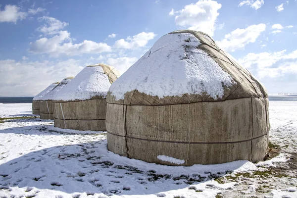 Yurts sob a neve no meio de um campo coberto de neve contra um céu com nuvens. viagem Quirguistão — Fotografia de Stock