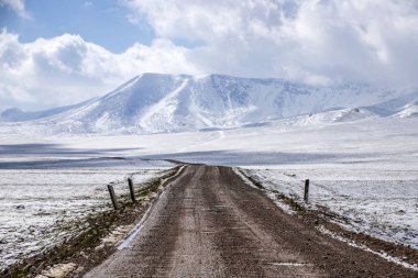 Karla kaplı otlaklar arasındaki yol, gökyüzüne bulutlarla doğru gidiyor. Kırgızistan'da seyahat