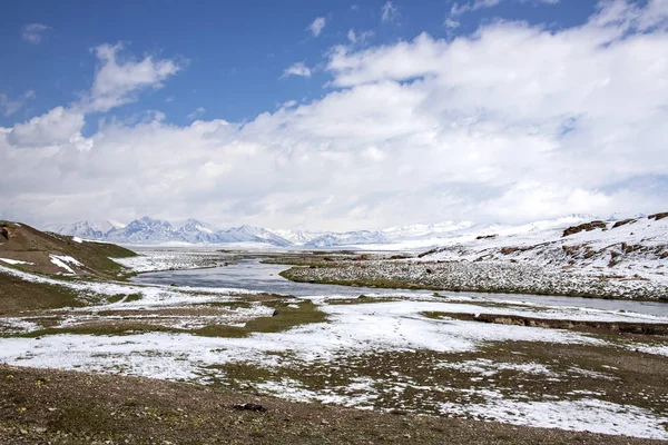 Älven mellan betesmarker täckta med snö. Vid horisonten finns en bergskedjan. Blå himmel i molnen — Stockfoto