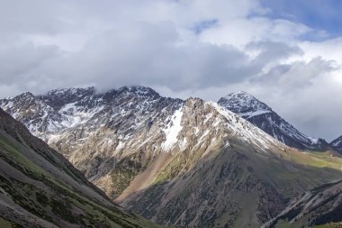 Bulutlu bir gökyüzüne karşı karla kaplı zirveleri ile dağ manzarası