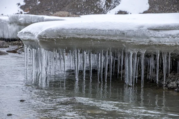 冰柱挂在河水上的雪石上 — 图库照片