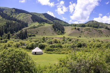 Orman ve gökyüzü ile kaplı dağların arka planına karşı jailoo üzerinde Beyaz yurt bulutlar ile. Issyk-Kul bölgesi