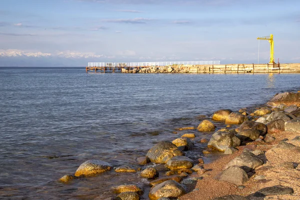 Side view of a pier on Issyk-Kul Lake with a mountain range with snowy peaks on the horizon