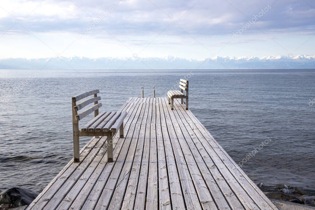 Pier with benches on Lake Issyk-Kul with a mountain range with snow-capped peaks on the horizon