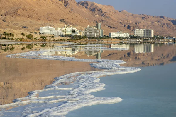 Reflektion av berg, hotell och palmer i Döda havets vatten med saltformationer — Stockfoto