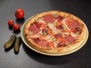 Bir tabakta salam, tavuk, domates ve salatalık turşusu ile Pizza