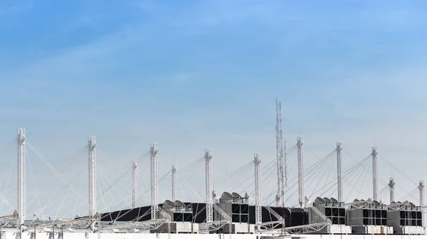 View on the roof of a building of a large air conditioning equipment with cable-suspended Swooping Rooftop Pylon Anchors, Pale Blue Summer Sky, Tied Suspension Roof Cables. Chiller.3