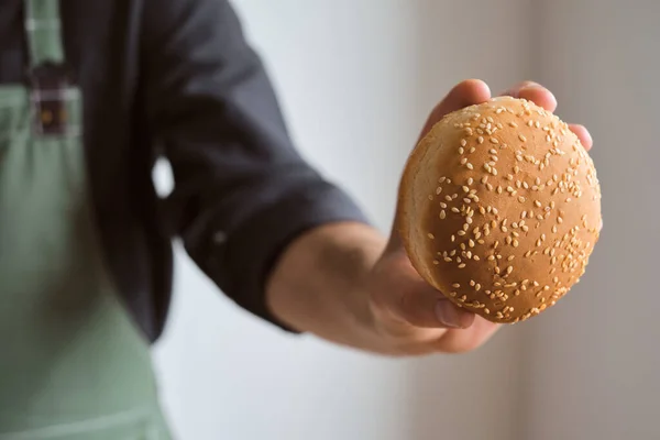 Burger buns in the hands of a man. Baking buns. Cooking hamburger, ingredient for the dish. Chef in an apron. Beautiful fresh buns with sesame seeds close-up. Traditional american delicious lunch