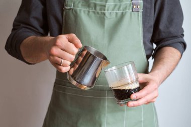 Barista kahve yapar. Adamın biri elinde süt sürahisi ve bir bardak kahve tutuyor. Adam cappuccino yapıyor, espressoya çırpılmış süt döküyor. Mutfak önlüklü barista. Profesyonel hizmet için ekipman