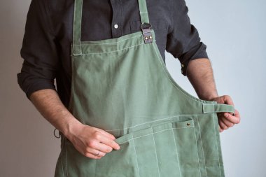 Mutfak önlüklü bir adam. Aşçıbaşı mutfakta çalışıyor. Üniformalı aşçı, koruyucu giysi. Yemek servisinde iş. Profesyonel aşçı. Yeşil kumaş önlük, günlük tarz kıyafetler. İş yerinde poz veren yakışıklı fırıncı