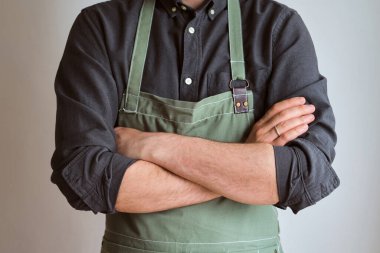 Mutfak önlüklü bir adam. Aşçıbaşı mutfakta çalışıyor. Üniformalı aşçı, koruyucu giysi. Yemek servisinde iş. Profesyonel aşçı. Yeşil kumaş önlük, günlük tarz kıyafetler. İş yerinde poz veren yakışıklı fırıncı