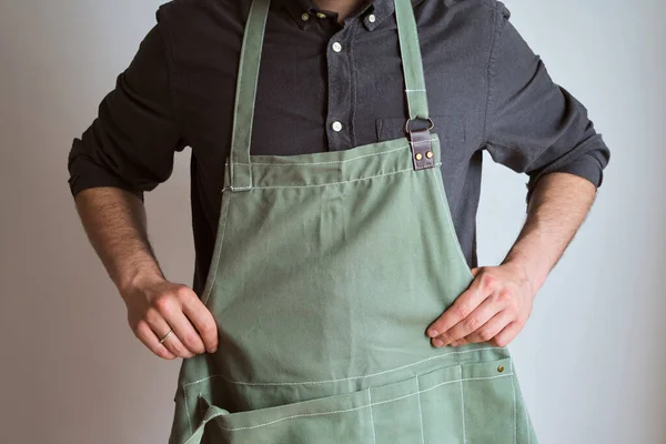 Mutfak önlüklü bir adam. Aşçıbaşı mutfakta çalışıyor. Üniformalı aşçı, koruyucu giysi. Yemek servisinde iş. Profesyonel aşçı. Yeşil kumaş önlük, günlük tarz kıyafetler. İş yerinde poz veren yakışıklı fırıncı