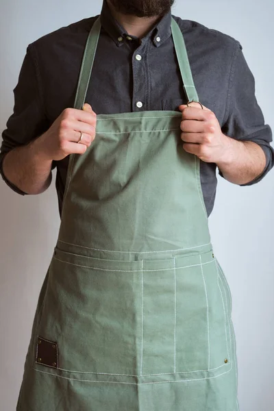 Mutfak önlüklü bir adam. Aşçıbaşı mutfakta çalışıyor. Üniformalı aşçı, koruyucu giysi. Yemek servisinde iş. Profesyonel aşçı. Yeşil kumaş önlük, günlük tarz kıyafetler. İş yerinde poz veren yakışıklı fırıncı
