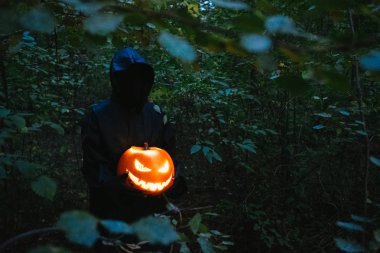 Elinde siyah bir adam Helluin kabak karanlık bir ormanda tutar.
