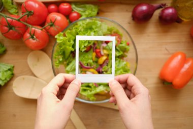 Polaroid fotoğraf çerçevesinden taze sebze ile ahşap masa üzerinde tutan eller.