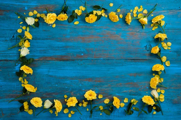 The composition of flowers. Frame made of yellow flowers on a blue wooden background. Easter, spring, summer concept. Flat lay, top vie