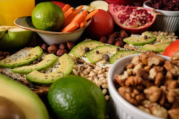 Crispbread with cheese and avocado, tomatoes, nuts, fruits, salad, spices on dark board background top view. Food and Health