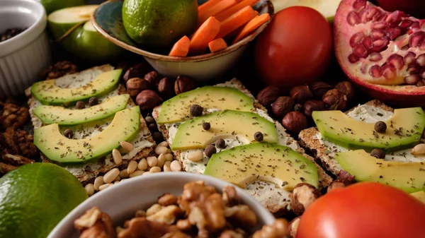 Crispbread with cheese and avocado, tomatoes, nuts, fruits, salad, spices on dark board background top view. Food and Health