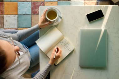 Kız bir defter, bir dizüstü bilgisayar ve telefon yanındaki notlar alır