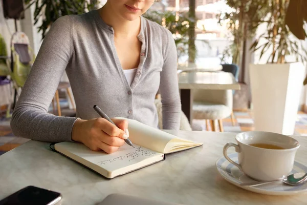 The girl takes notes in a notebook, next to a laptop and phone