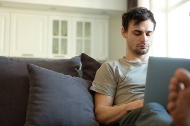 Bin yıllık adam sosyal ağlardan takipçileri ile genç erkek şık mobilyalar ile modern ev iç onun boş vakit mesajlaşma için vakit dizüstü bilgisayar ile kanepede yatan