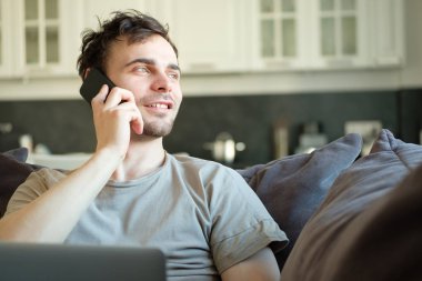 Bin yıllık adam sosyal ağlardan takipçileri ile genç erkek şık mobilyalar ile modern ev iç onun boş vakit mesajlaşma için vakit dizüstü bilgisayar ile kanepede yatan