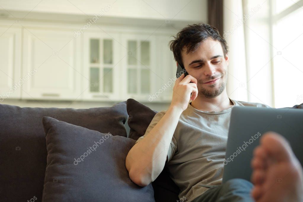 Millennial man lying on sofa with laptop computer spending time for messaging with followers from social networks, young male spending his leisure time in modern home interior with stylish furniture