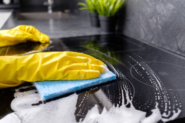 Kız mavi sünger ocakla sarı eldiven yıkar.