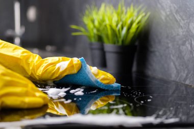 The girl washes the stove with a blue sponge in yellow gloves clipart