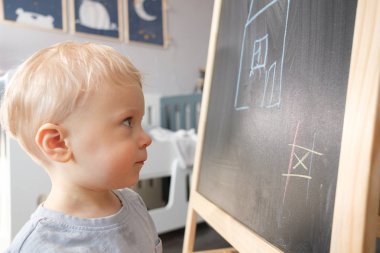 Çocuk evde boya kalemi ile tahtaya çizer.