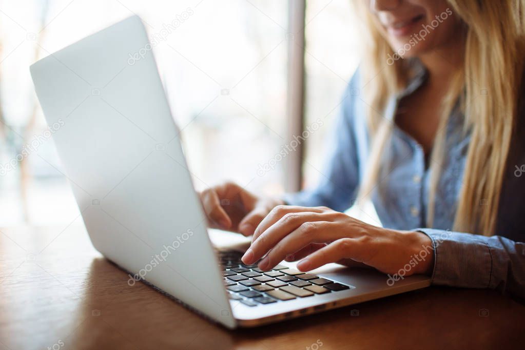 Young woman working in a cafe, keyboard on a laptop computer. Blond student working for netbook after lectures at the university.