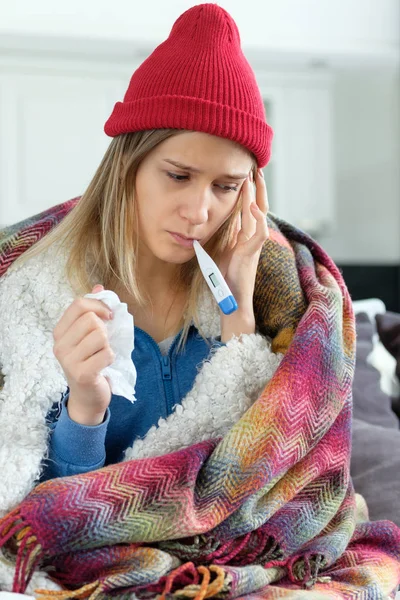 The girl is sick at home, wrapped in a blanket and a thermometer in the mouth