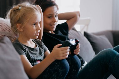 Çocuklar evdeki konsolda joystickle oynuyorlar.