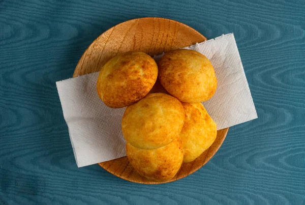 Tipik Kolombiya almojabanalarının üst görüntüsü, geleneksel Kolombiya peynirli ekmek ahşap bir tabağın üzerinde mavi arka planda peçeteyle. Geleneksel fırın