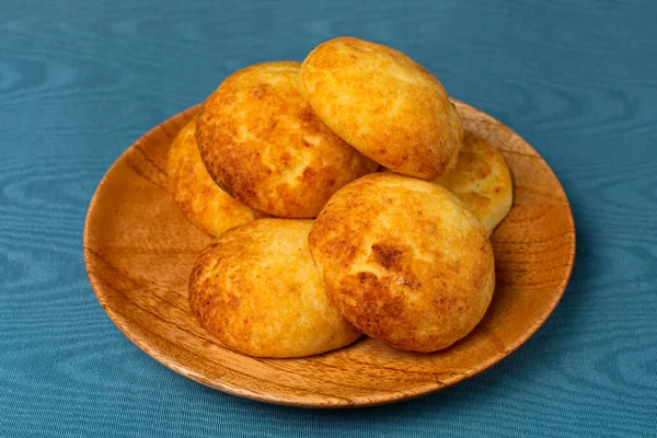 Tipik Kolombiya almojabanaları, geleneksel Kolombiya peyniri ekmeği mavi arka planda bir ahşap tabağın üzerinde. Geleneksel fırın