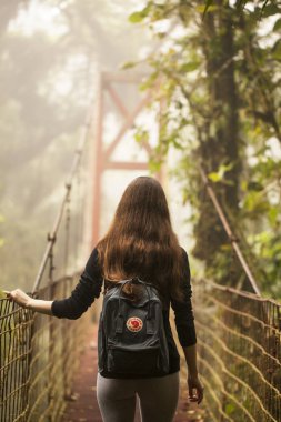 Monteverde,Puntarenas/Costa Rica-24 January,2019:young traveler hiking in Monteverde Claude forest with a practical Fjallraven Kanken backpak. Swedish company specializing in outdoor equipment. clipart