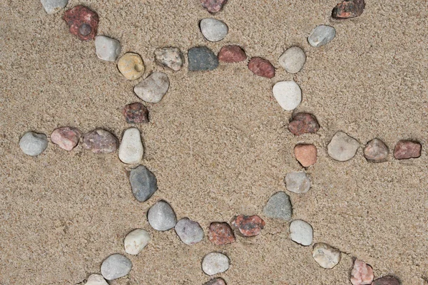 sun shape made of pebble stones on sand background