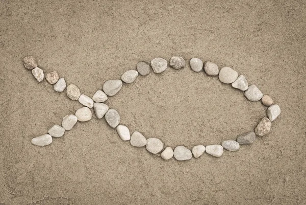 Christian symbol  - fish shapemade of stones on sand — Stock Photo, Image