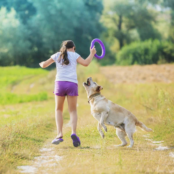 一个带着狗的年轻女孩在田野里的一条乡村路上跑 女孩手里拿着一枚训练戒指 — 图库照片